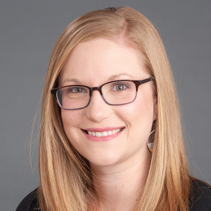 A headshot of Andria, a white woman with blonde hair. She is wearing glasses and smiling at the camera.